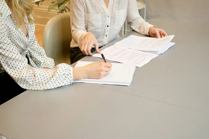 Două persoane care completează și semnează acte la o masă